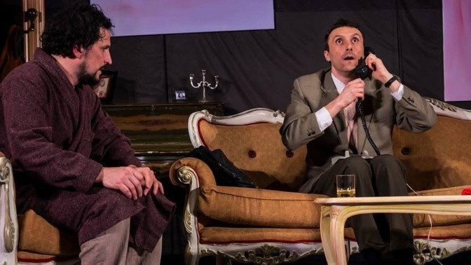 Scena dello spettacolo La cena dei cretini di On Art a Brescello, con Matteo Bartoli e un altro attore seduti in salotto, durante un esilarante equivoco telefonico.